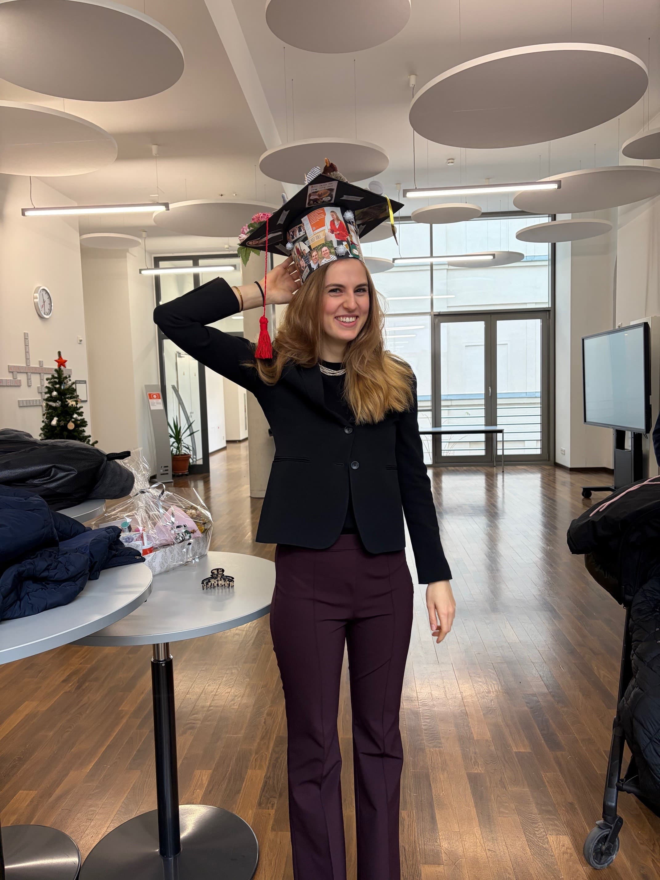 Julia Thomas standing in the iwm foyer wearing a decorated doctoral cap after her dissertation defense.